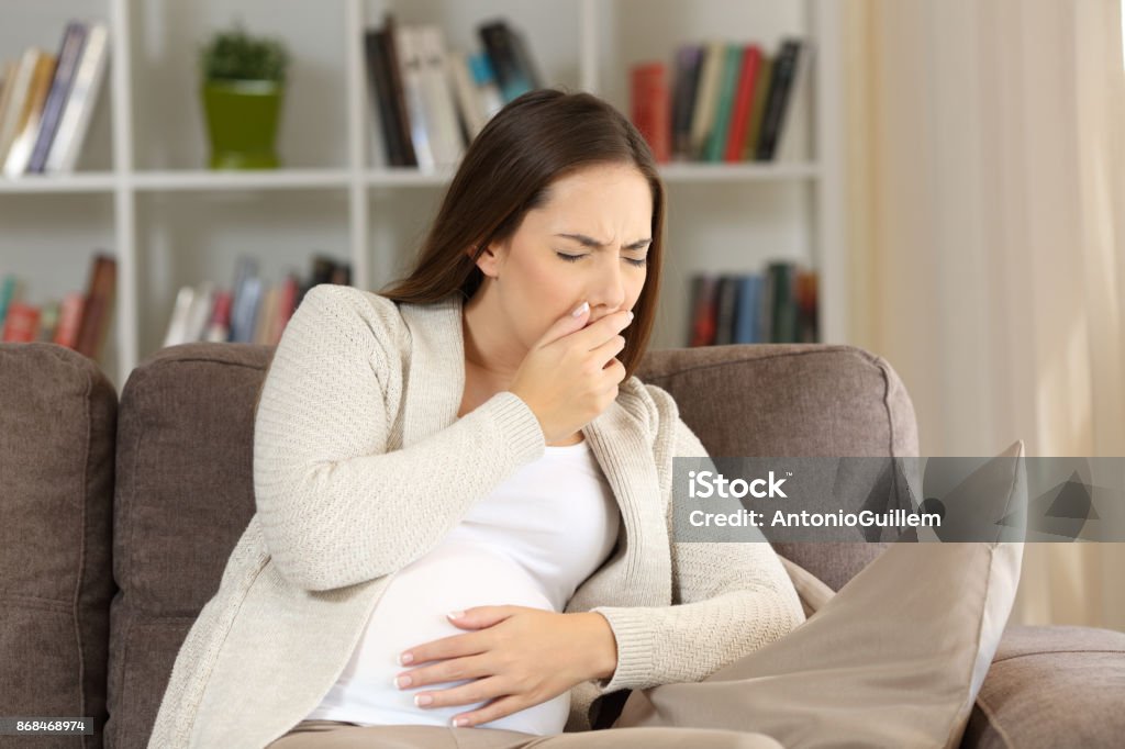 Pregnant woman with nausea at home Pregnant woman suffering nausea sitting on a sofa at home Confusion Stock Photo