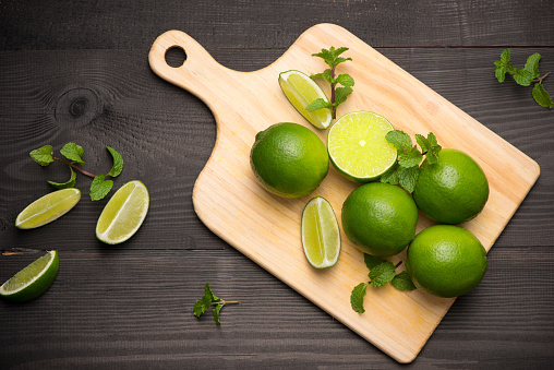 Fresh limes on cutting board on wooden table with spoon of salt. Top view, background.
