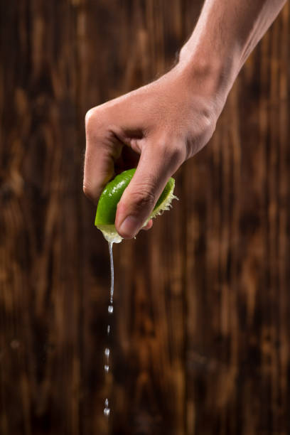 Hand squeeze lime with lime drop on dark wooden background