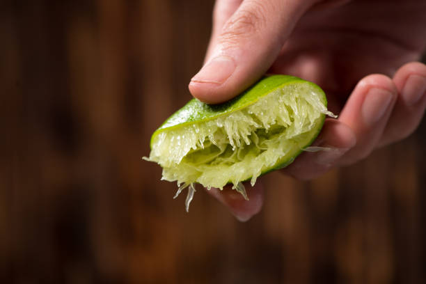 istock Hand squeeze lime with lime drop on dark wooden background 868482812