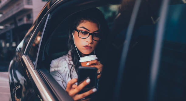 женщина-предприниматель с кофе смотреть подкаст на смартфоне в лимузине - luxury car women smart phone стоковые фото и изображения