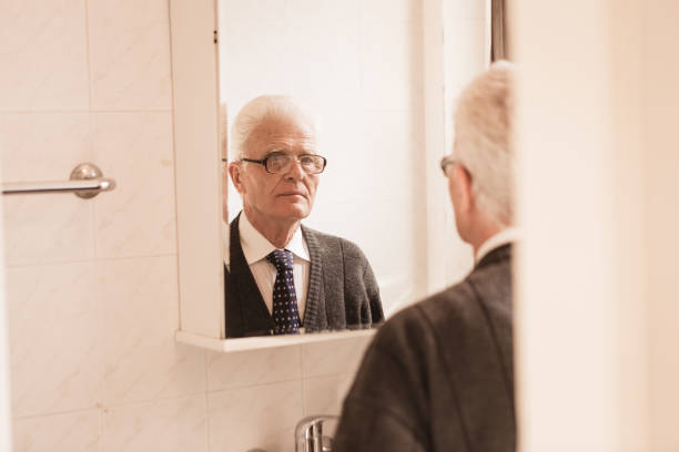 istock Seniors at Home. Senior man looking in bathroom mirror buttoning his tie 868483938