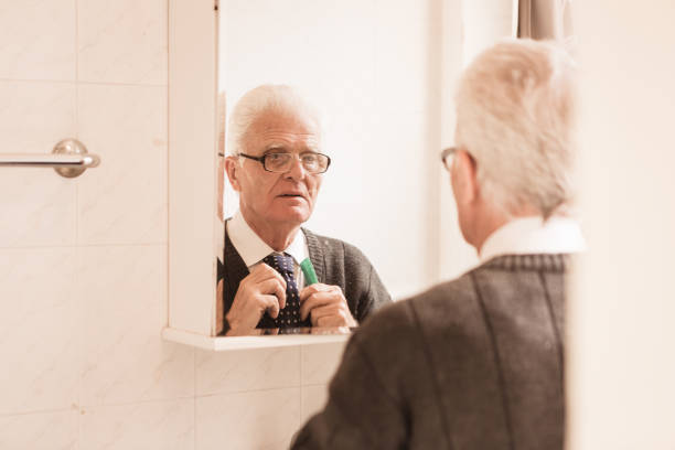 istock Seniors at Home. Senior man looking in bathroom mirror buttoning his tie 868483950