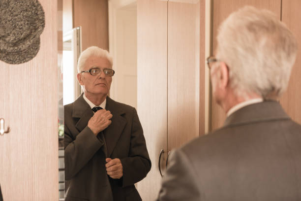 istock Seniors at Home. Senior man looking himself at the mirror, getting dresses, buttoning his tie 868484092