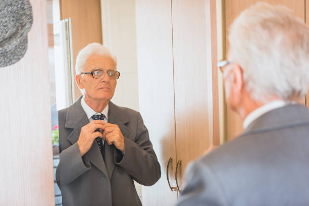 istock Seniors at Home. Senior man looking himself at the mirror, getting dresses, buttoning his tie 868484214