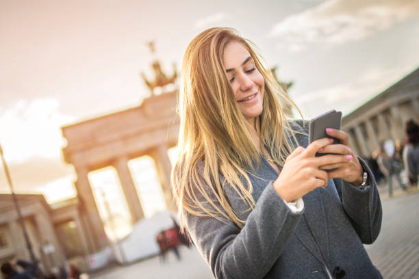 istock Smiling young woman using phone in front front of Brandenburg gate, Berlin, Germany. 868484354