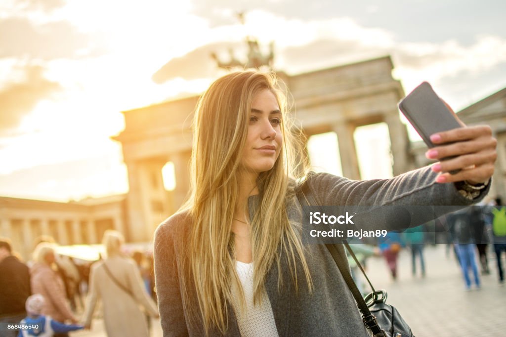 Beautiful young woman taking selfie photo in front of Brandenburger Tor in Berlin at sunset. Brandenburg Gate Stock Photo