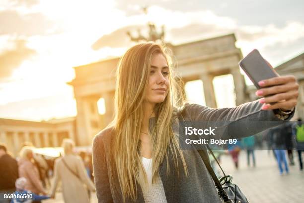 Beautiful Young Woman Taking Selfie Photo In Front Of Brandenburger Tor In Berlin At Sunset Stock Photo - Download Image Now