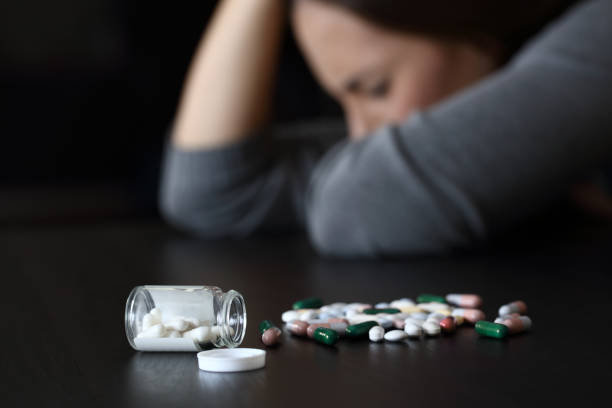 Depressed woman beside a lot of pills Close up of a depressed woman beside a lot of pills on a table on a dark background Substance Abuse stock pictures, royalty-free photos & images