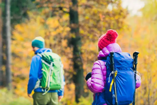 Happy couple hikers trekking in beautiful yellow autumn forest and mountains. Young people man and woman walking on trek trail with backpacks, healthy lifestyle adventure, camping on hiking trip.