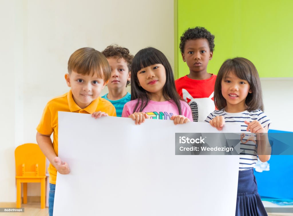 Vielfalt Kinder halten leere Plakat im Klassenzimmer im Kindergarten Vorschule, verspotten Multiethnic Gruppe mit Schild, zum Hinzufügen von Text oder design - Lizenzfrei Vorschulalter Stock-Foto