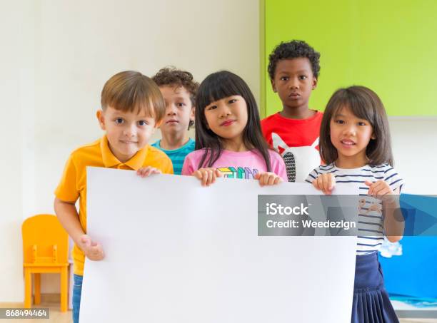 Diversity Children Holding Blank Poster In Classroom At Kindergarten Preschool Multiethnic Group With Sign Board Mock Up For Adding Text Or Design Stock Photo - Download Image Now