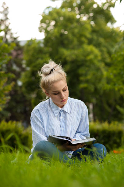 istock Young woman sitting on grass and reading book 868495068