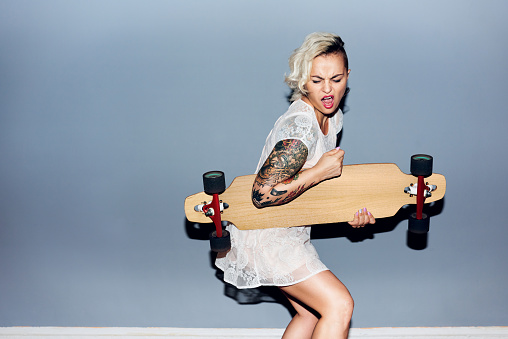 Tattooed pretty blond girl goofing around, playing longboard as guitar and singing