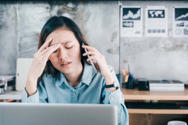 kreative designer asiatin abdeckung ihr gesicht mit hand und fühlen sich aufgeregt beim sprechen auf handy mit kunden vor laptop-computer am schreibtisch im büro, stress-büro-lifestyle-konzept betont - frustration office worker women business stock-fotos und bilder