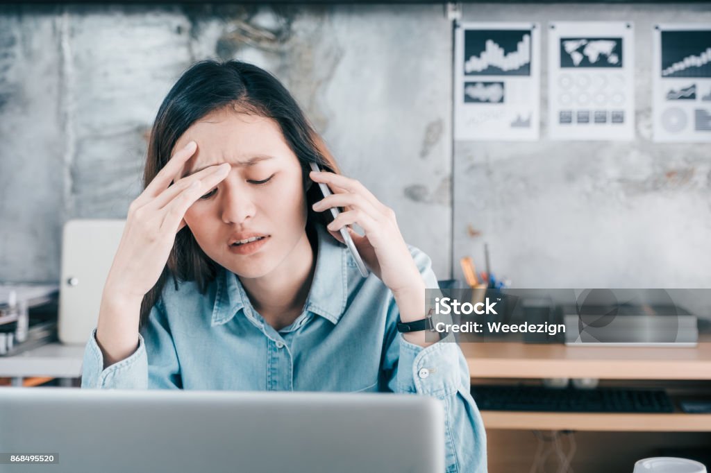 Stressed Asian creative designer woman cover her face with hand and feel upset while talk on mobile phone with customer in front of laptop computer on desk at office,Stress office lifestyle concept Stressed Asian creative designer woman cover her face with hand and feel upset while talk on mobile phone with customer in front of laptop computer on desk at office,Stress office lifestyle concept. Using Phone Stock Photo