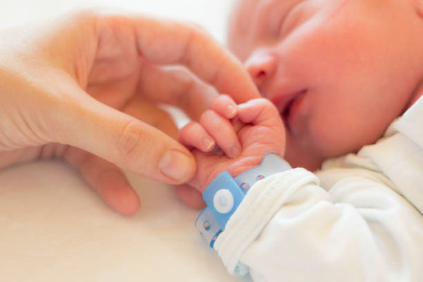 The Strongest Connection Newborn baby boy sleeping in his crib, his mother's hand holding his little hand. new baby stock pictures, royalty-free photos & images