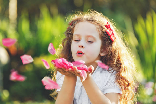 Little girl blowing rose petals from her hands. Fresh, healthy respiration concept.