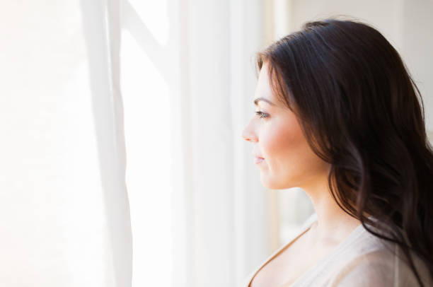 istock young woman looking through window at home 868535530