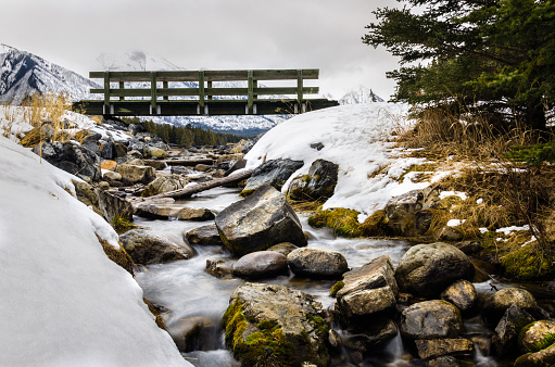 Photo of a Small Wooden Pedestrian Bridge Spanning a Mountain Creek on a Cloudy Winter Day.