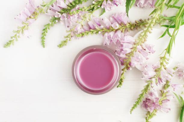 Jar of skin and body care cream framed fresh violet flowers top view white surface, light delicate faded tones. botanical spa treatment stock pictures, royalty-free photos & images