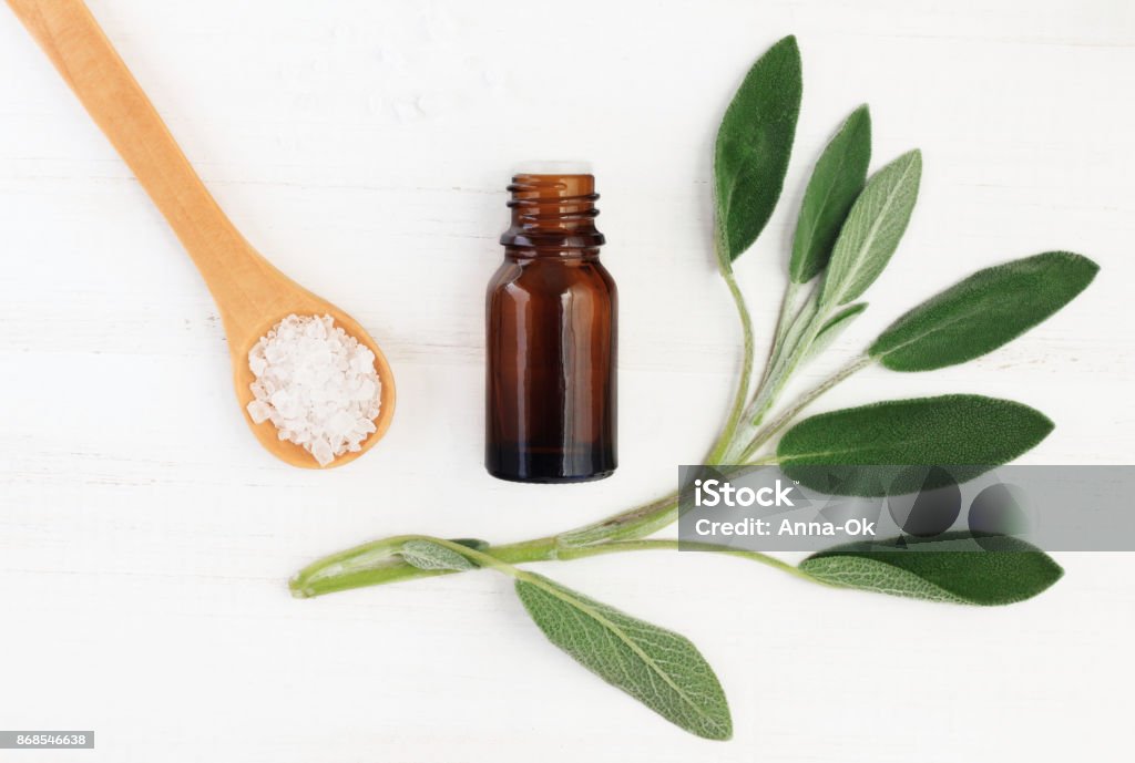 Salvia officinalis essential oil and sea salt for natural skincare top view. Green fresh leaves, dropper bottle, holistic ingredients. Sage Stock Photo