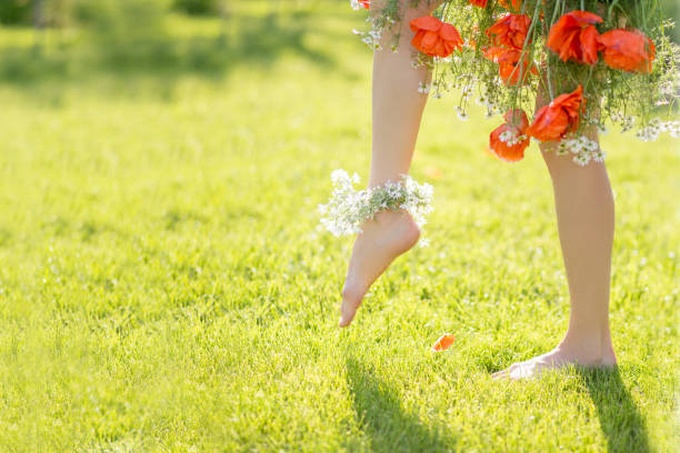Spring is coming concept. Beautiful woman legs barefoot wearing floral dress waling on a sunny meadow