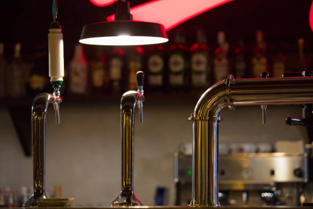 bar counter with beer taps and lamp on wall background with bottles