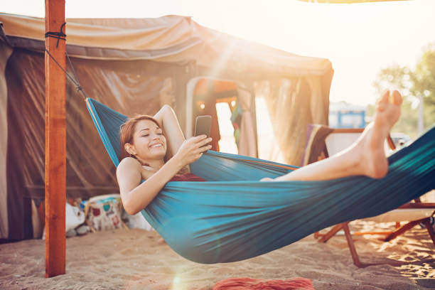Relaxation and communication Young woman with smart phone resting in a hammock hammock stock pictures, royalty-free photos & images