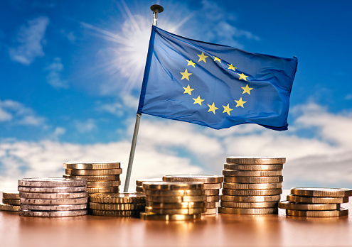European flag with stacks of euro coins in front of a blue sky