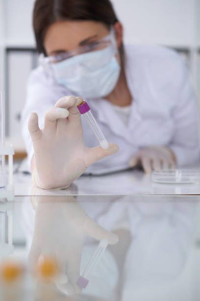 close-up of professional female scientist in protective eyeglasses making experiment with reagents in laboratory. medicine and research concept - close up medical test exam people imagens e fotografias de stock