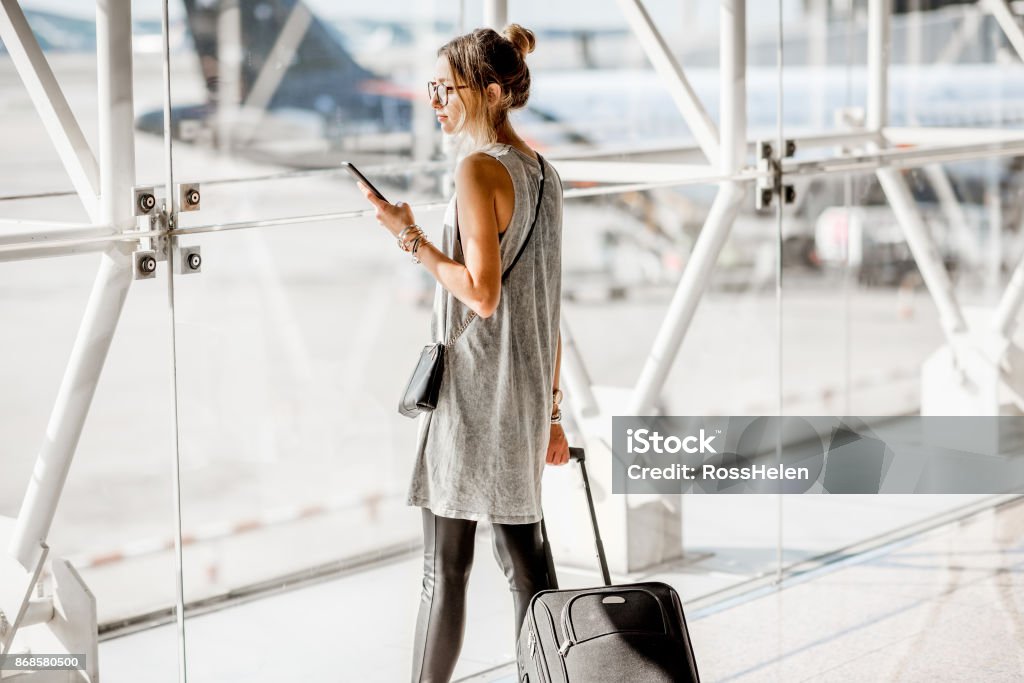 Woman at the airport Young woman standing with phone near the airport window waiting for the flight Airport Stock Photo