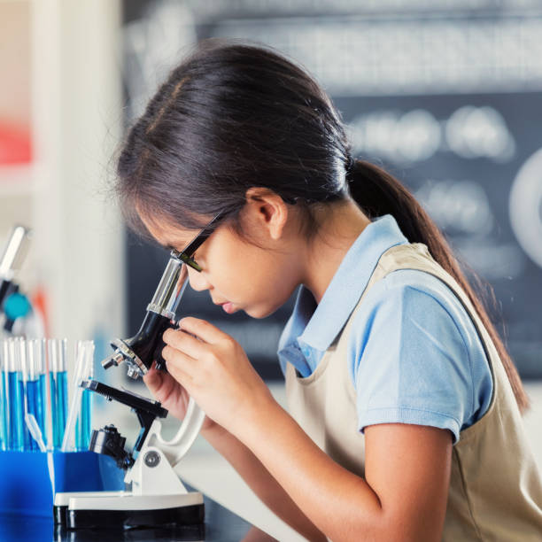 istock Young girl looks through microscope at school 868595614