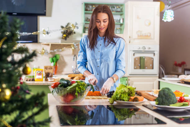 Young Caucasian lady cooking New Year or Christmas meal in decorated kitchen at home Young Caucasian lady cooking New Year or Christmas meal in decorated kitchen at home. woman making healthy dinner stock pictures, royalty-free photos & images