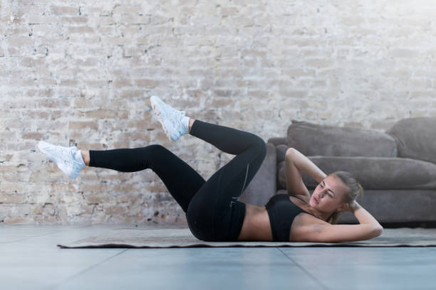 giovane donna sportiva che fa esercizio crunch incrociato sdraiato su un tappeto nello studio moderno - crisscross foto e immagini stock