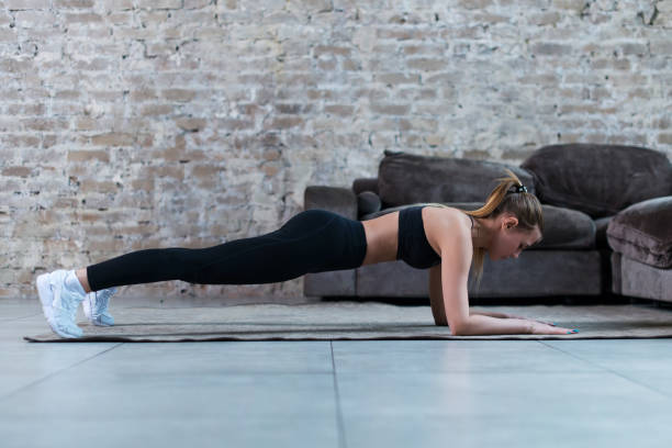 istock Slim young brunette wearing black gym clothing doing abdominal bridge or front plank exercise in loft apartment. 868604082