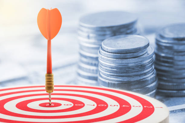 istock Red dart hit in the center of a target with stack of coins behind. 868604220
