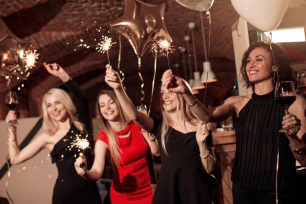 Group of happy smiling girlfriends wearing evening dresses celebrating New Year holding sparklers in decorated cafe Group of happy smiling girlfriends wearing evening dresses celebrating New Year holding sparklers in decorated cafe. cocktail dress stock pictures, royalty-free photos & images