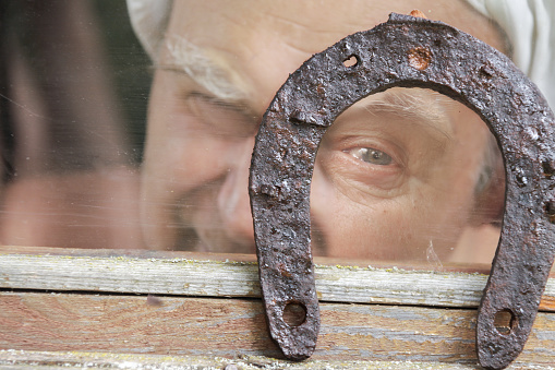 Face of one senior adult man looking through luck horseshoe - Symbol of the fortune close-up.