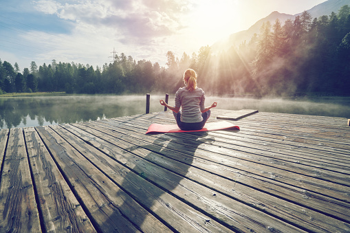 Caucasian girl exercising yoga in nature, morning by the lake in Switzerland