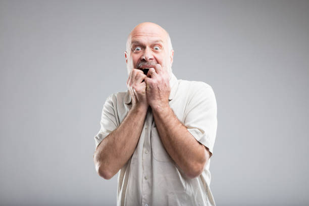 scared man biting his nails because of fear frightened old man in an exaggerated expressino of fear - studio portrait on neutral background caricature photos stock pictures, royalty-free photos & images