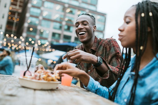 A group of friends have fun spending time in New York city, exploring Manhattan together.  They eat at a large food truck area downtown called Smorg Square, enjoying various kinds of street food.