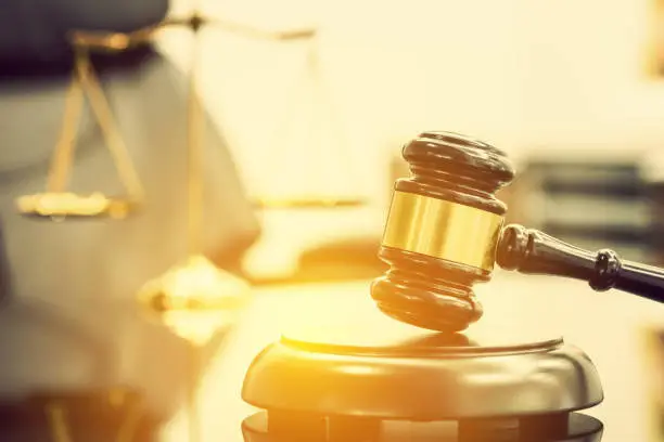 Legal office of lawyers, justice and law concept : Wooden judge gavel or a wood hammer and a soundboard used by a judge person on a desk in a courtroom with a blurred brass scale of justice behind.