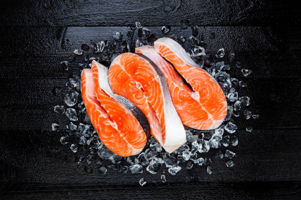 Fresh raw salmon red fish steak on ice on black wooden table top view