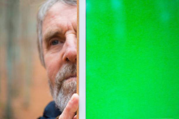 Senior Man Holding Digital Tablet with Green Screen and Hiding Half of his Face, Autumnal Beech Forest, Europe Senior man holding digital tablet with green screen in front and hiding half of his face in autumnal beech forest, Europe. person holding frame over face stock pictures, royalty-free photos & images