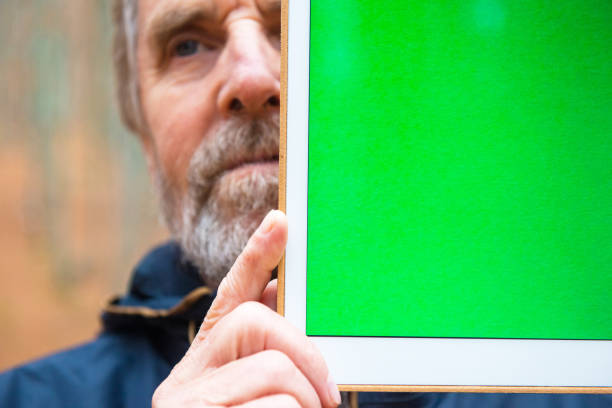 Senior Man Holding Digital Tablet with Green Screen and Hiding Half of his Face, Autumnal Beech Forest, Europe Senior man holding digital tablet with green screen in front and hiding half of his face in autumnal beech forest, Europe. person holding frame over face stock pictures, royalty-free photos & images