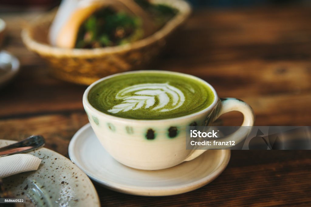 Close-up - ceramic cup with green tea called Matcha Close-up - ceramic cup with green tea with milky foam with beautiful pattern on the background of blurry basket with food Alcohol - Drink Stock Photo