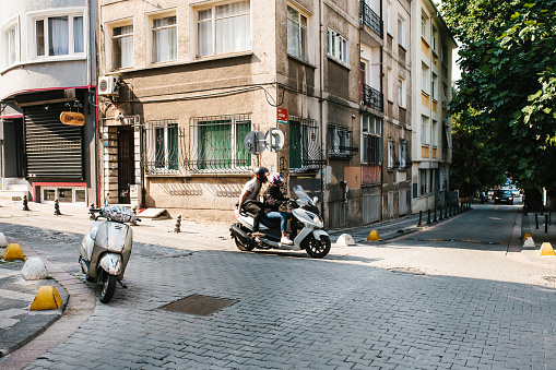 Istanbul, June 14, 2017: Two people ride scooter past an empty parked moped in Istanbul on warm summer day