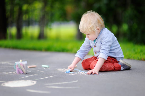 istock Happy little kid boy sitting and drawing with colored chalk on asphalt 868679428