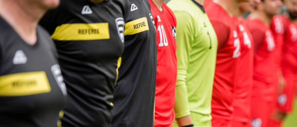 Football team in red uniform and three referees standing in a row during national anthem.